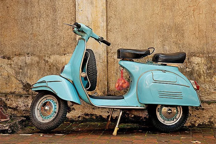 Vespa d'epoca azzurra parcheggiata davanti a un muro