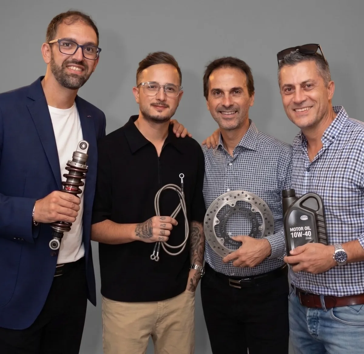 Lo staff di CIR Moto, da sinistra: Stefano con un ammortizzatore, Nicola con un tubo freno in treccia, Alessio con un disco freno e Andrea con una tanica di olio motore